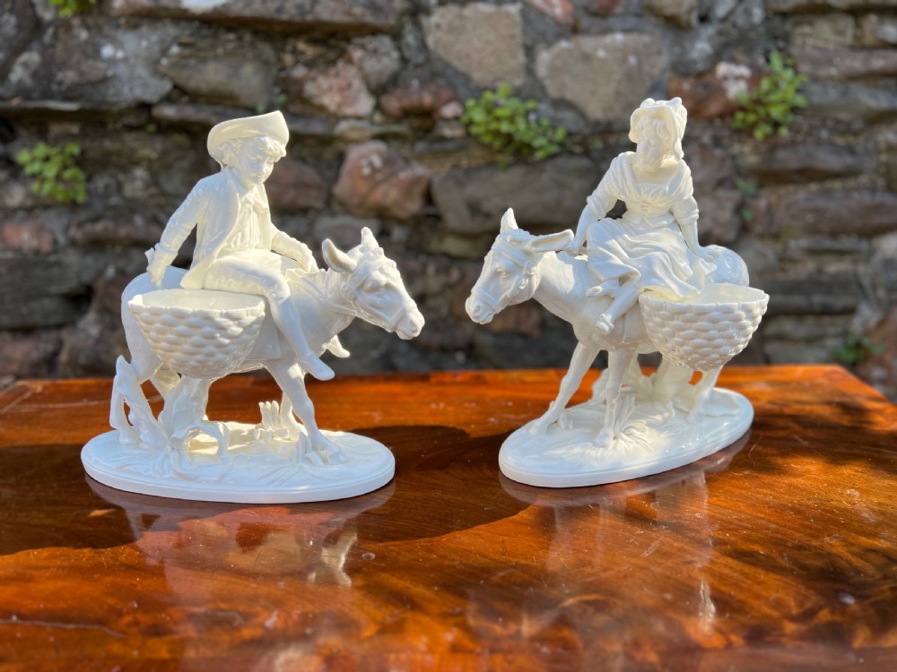 pair of porcelain figures by moore bros depicting a man and a woman riding donkeys